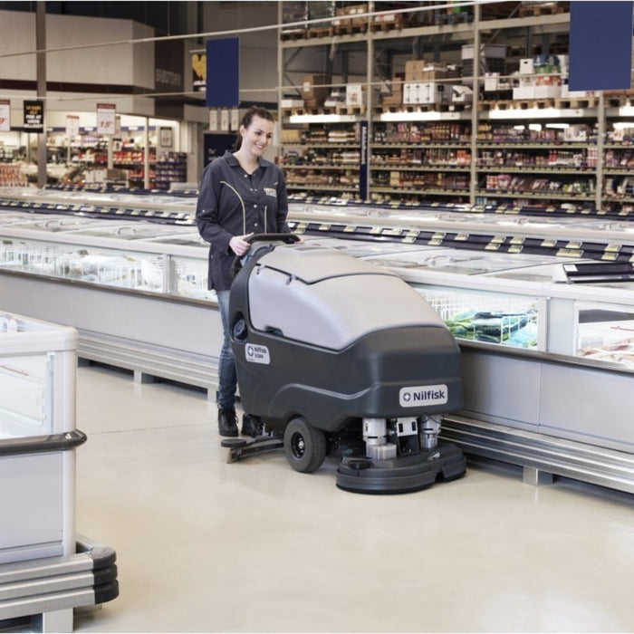 Employee operating Nilfisk SC800 71 large walk-behind scrubber dryer for efficient commercial floor cleaning in a supermarket