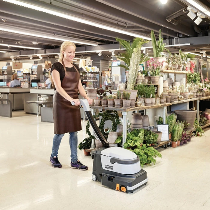 Person using a floor cleaning machine in a store with plants and customers in the background