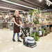 Person using a floor cleaning machine in a store with plants and customers in the background
